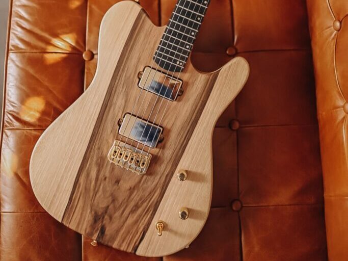 guitare électrique en bois clair posée sur un canapé couleur cognac