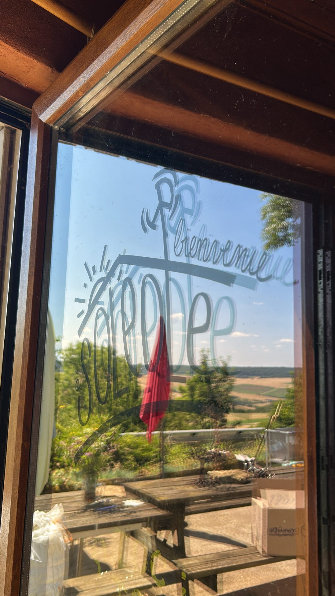 Une porte vitrée sur laquelle est floqué le logo du Gite Soleole en arrière plan les champs de la campagne lorraine